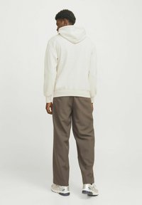 Sweatshirt à capuche blanche avec poche kangourou, associé à un pantalon ample marron et des chaussures de sport argentées. Texture subtile, aucun motif visible.