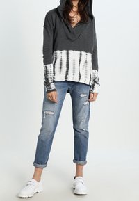 Bluza z kapturem z głębokim dekoltem w serek, ciemnoszara góra i biały dolny element w stylu tie-dye; połączona z podartymi jasnoniebieskimi dżinsami i białymi trampkami.