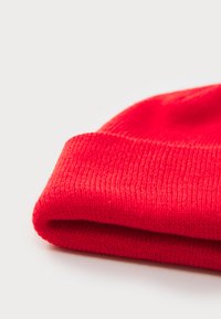Red knit beanie with a soft texture, featuring a rolled cuff and even stitching pattern. Material appears warm and stretchable.