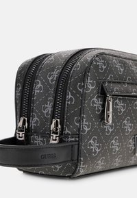 Szara torebka na kosmetyki w wzory z podwójnymi suwakami, teksturowanym materiałem i czarnymi akcentami. Na boku wytłoczona nazwa marki „GUESS”.