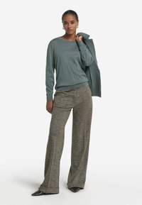 Jasnozielony sweter z okrągłym dekoltem, zestawiony z szerokimi spodniami w brązowe i beżowe wzory, uzupełniony czarnymi szpilkami.