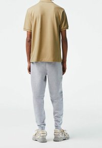 Polo shirt beige, pantalon de jogging gris et baskets grises. La chemise a des manches courtes ; le pantalon présente une texture côtelée et un design à jambes fuselées.