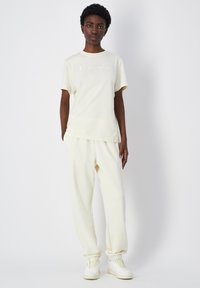 Light beige Champion t-shirt with embroidered logo, paired with matching tapered sweatpants, featuring elastic cuffs and a smooth, soft texture.