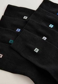 Musta sukat järjestettyinä kerroksittain, joissa on ribattu pinta. Jokaisessa on pieni, värikäs brodeerattu logo reunassa vaihtelevissa sävyissä.