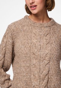 Beiger Strickpullover mit Zopfmuster und geripptem Halsausschnitt, ausgestattet mit strukturierten Details und klassischer Passform.