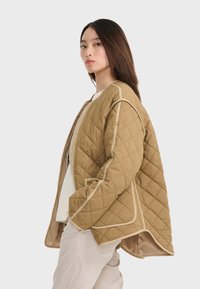 Gepolsterte beiges Außenjacke mit kontrastierendem helleren Besatz, Druckknöpfen vorne und einem lockeren Schnitt. Verfügt über ein Übergrößendesign und seitliche Taschen.
