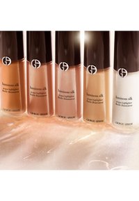 Vijf flessen van de Giorgio Armani Luminous Silk highlighter in verschillende tinten van goud tot wit, met slanke zwarte doppen en heldere bases.
