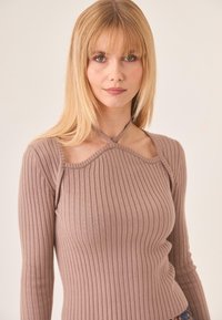 Mujer rubia con el cabello liso que lleva una blusa de manga larga de canalé en color malva con un escote con corte y tirantes de halter.