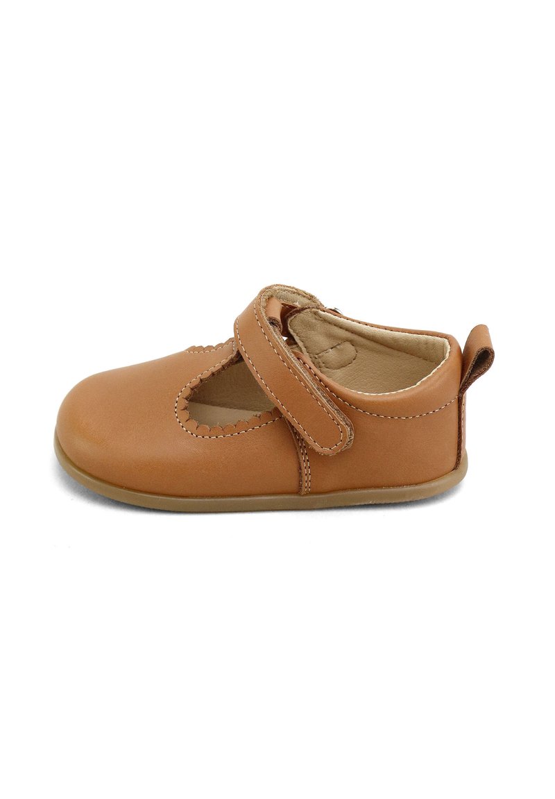 Zapato de cuero en tono marrón claro con punta redondeada y diseño recortado. Presenta una correa de velcro y una suela de goma texturizada.
