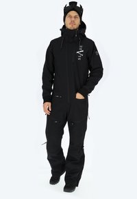 Completo da sci nero con chiusura zip frontale, polsini regolabili e numerose tasche con zip. Presenta un logo sul petto e un materiale caldo.