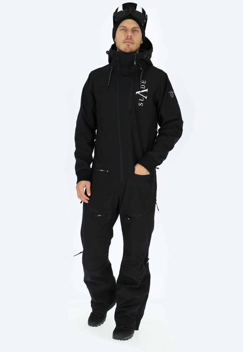 Completo da sci nero con chiusura zip frontale, polsini regolabili e numerose tasche con zip. Presenta un logo sul petto e un materiale caldo.