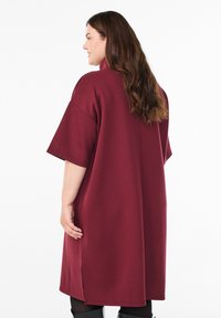 Burgundy oversizeklänning med korta ärmar, tillverkad av mjukt tyg, med sidorevor och en avslappnad silhuett.