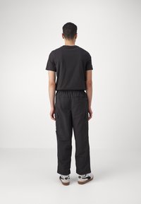 Zwarte T-shirt met korte mouwen, gecombineerd met losse zwarte cargo-broeken. De outfit heeft een ontspannen pasvorm en een elastische tailleband, met zijzakken.
