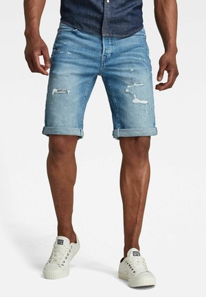 Lichtblauwe denim shorts met gescheurde accenten en opgerolde zoom, gecombineerd met witte sneakers met een gestructureerde zool en veters.
