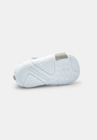 White sneaker with a textured rubber outsole, smooth upper material, circular tread pattern, and cushioned heel tab. Features embossed branding.