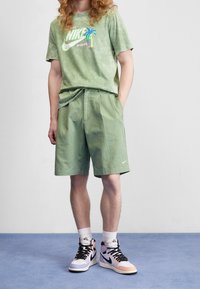 Jasnozielona koszulka Nike w tie-dye z grafiką palmowego drzewa, zestawiona z pasującymi zielonymi szortami i wielokolorowymi butami na wysokiej podeszwie.