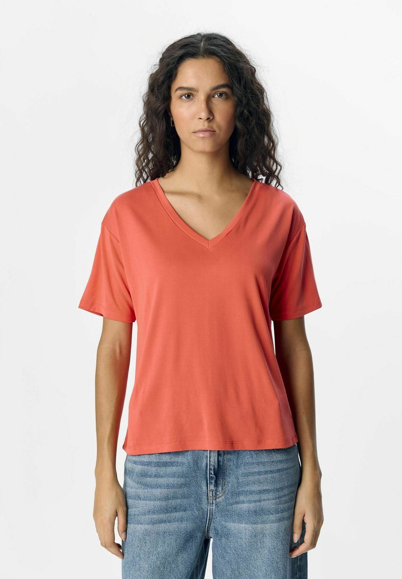 Korallfarvet V-hals t-shirt lavet af blødt stof med korte ærmer, med en afslappet pasform og en glat overflade. Sammen med lyseblå jeans.