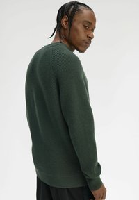 Maglione verde lavorato a maglia con una trama a coste, caratterizzato da maniche lunghe e scollo a girocollo. Il design presenta una vestibilità comoda e cuciture sottili.