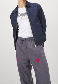 Jeansjacka i marinblått, med dragkedja fram och sidofickor. Under finns en vit t-shirt med grå design. Grå byxor med röda broderiaccenter.