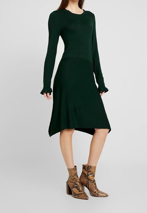 Robe verte à manches longues avec un col volanté et un ourlet asymétrique, associée à des bottines chelsea à imprimé serpent brun avec un talon bloc.