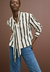 Stribet bluse i creme og sort med en knyttet krave, lange ærmer og en afslappet pasform, parret med blå høj talje jeans.
