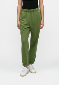 Green sweatpants with an elastic waistband and cuffed ankles, made from a soft material and featuring a relaxed fit. Worn with white sneakers.