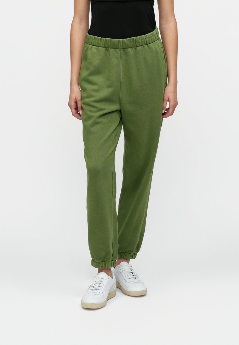 Green sweatpants with an elastic waistband and cuffed ankles, made from a soft material and featuring a relaxed fit. Worn with white sneakers.