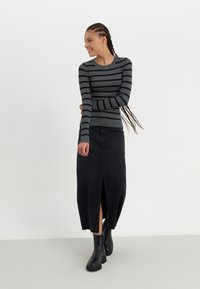 Jupe en denim noir avec fente à l'avant et un haut tricoté gris à rayures à manches longues. Texture lisse, design ajusté et motifs côtelés sur les manches.