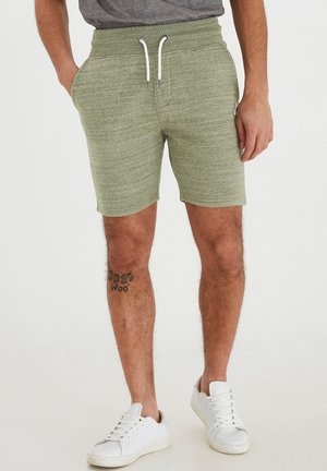 Lichtgroene, textuur atletische shorts met een elastische tailleband, met trekkoordsluiting en zijzakken. Draagt witte sneakers.
