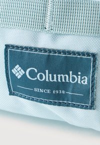 Ετικέτα μάρκας Columbia με λευκό κείμενο σε μπλε ύφασμα, ραμμένη σε ανοιχτό μπλε υφαντό υλικό, με την ένδειξη "Από το 1938".