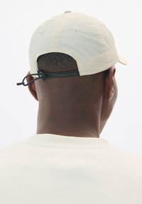 Beige színű baseball sapka lekerekített koronával, hátul állítható pánttal és strukturált anyaggal. A háttér sima fehér.