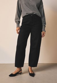Sorte højtaljede jeans med løs pasform, kombineret med en grå langærmet sweater og sorte slingback hæle. Glat stoftekstur.