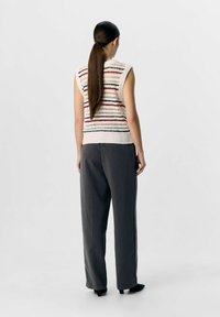 Débardeur en tricot crème avec des rayures horizontales multicolores et un motif ajouré, associé à un pantalon large gris.