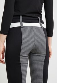 Zwarte en grijze broek met een hounsdtoothpatroon aan de zijkanten, voorzien van een witte tailleband en stoflussen, gestroomlijnd ontwerp, aansluitende snit.