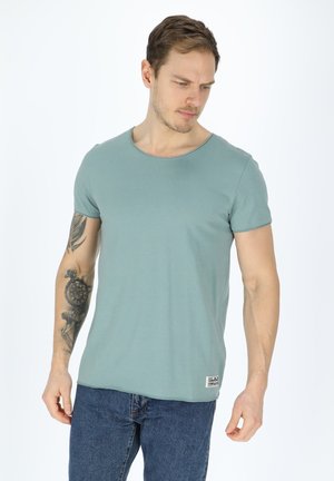 Green cotton t-shirt with a round neckline and short sleeves, featuring a subtle texture. Paired with blue denim jeans.