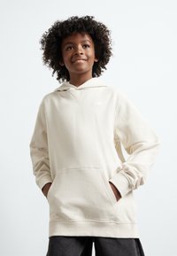 Beige kapucnis pulóver elöl zsebes, húzózsinórral ellátott kapucnival és bordás mandzsettával. A felső mell részen kis fehér logó található. Puha tapintású.