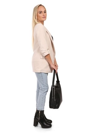 Blazer rose clair avec manches retroussées, associé à un jean bleu clair et des bottines noires à talons. Portant un sac fourre-tout noir avec un détail en forme de frange.