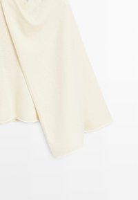 Pull en mélange de laine couleur crème avec une texture douce, un design fluide et un ourlet courbé. Présente une coupe décontractée et des manches longues.