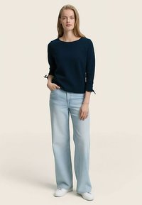 Granatowa bluzka z długim rękawem, okrągłym dekoltem i wiązaniami na rękawach, zestawiona z jasnoniebieskimi szerokimi spodniami i białymi trampkami.