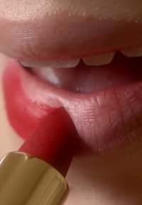 Red lipstick being applied to lips. The lipstick has a matte finish, and the tube features a gold accent at the base. Smooth, defined lips.