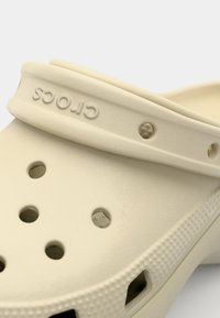 Sabots Crocs beiges en matériau léger, avec des trous d'aération, une bride arrière surélevée et une surface texturée avec détail logo.