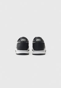 Des chaussures de sport noires au design épuré, avec une semelle intermédiaire blanche et des accents gris. Le logo est affiché de manière proéminente au niveau du talon.