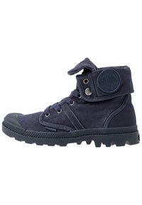 Botas de tobillo de lona azul marino con puntera de goma, diseño con cordones y puño ajustable de velcro que presenta un parche circular con logo en el lateral.