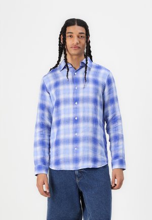 Blue plaid long-sleeve shirt featuring varying shades of blue with a button-down front and soft, textured fabric. Paired with denim shorts.