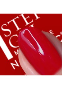 Lys rød neglelakk på en glatt, ovalformet negl, nærbilde med en blank finish. Bakgrunnen har hvit tekst på en rød overflate.