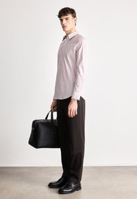 Lichtroze gestreepte lange mouwen shirt, zwarte broek, zwarte leren schoenen, houdend een zwarte leren tas, staand op een gladde vloer.