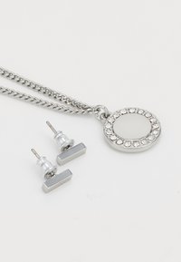 Collana d'argento con un pendente rotondo decorato con strass. Comprende orecchini a perni rettangolari coordinati, il tutto in una finitura metallica lucida.