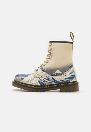 Sznurowane botki za kostkę z kremowego płótna z niebieskimi wzorami fal, wyposażone w czarną gumową podeszwę i żółte przeszycia. Tkaninowa pętla z tyłu.