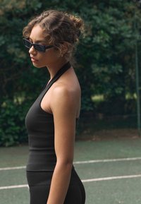 Top nero senza maniche a coste con design a collo all'americana, abbinato a pantaloni coordinati a coste. Il modello indossa occhiali da sole rettangolari neri.