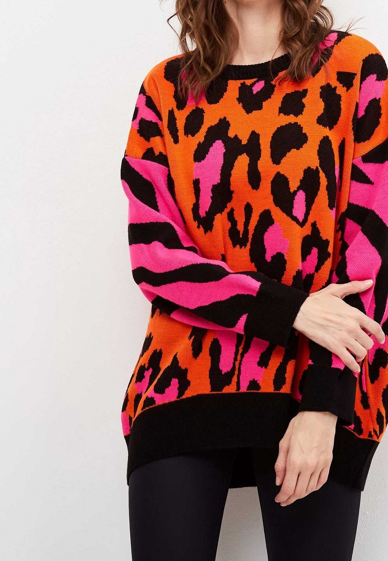 Pull en maille avec une base orange ornée de motifs léopard noirs et roses, poignets noirs, et coupe décontractée. Tissu texturé, manches longues.